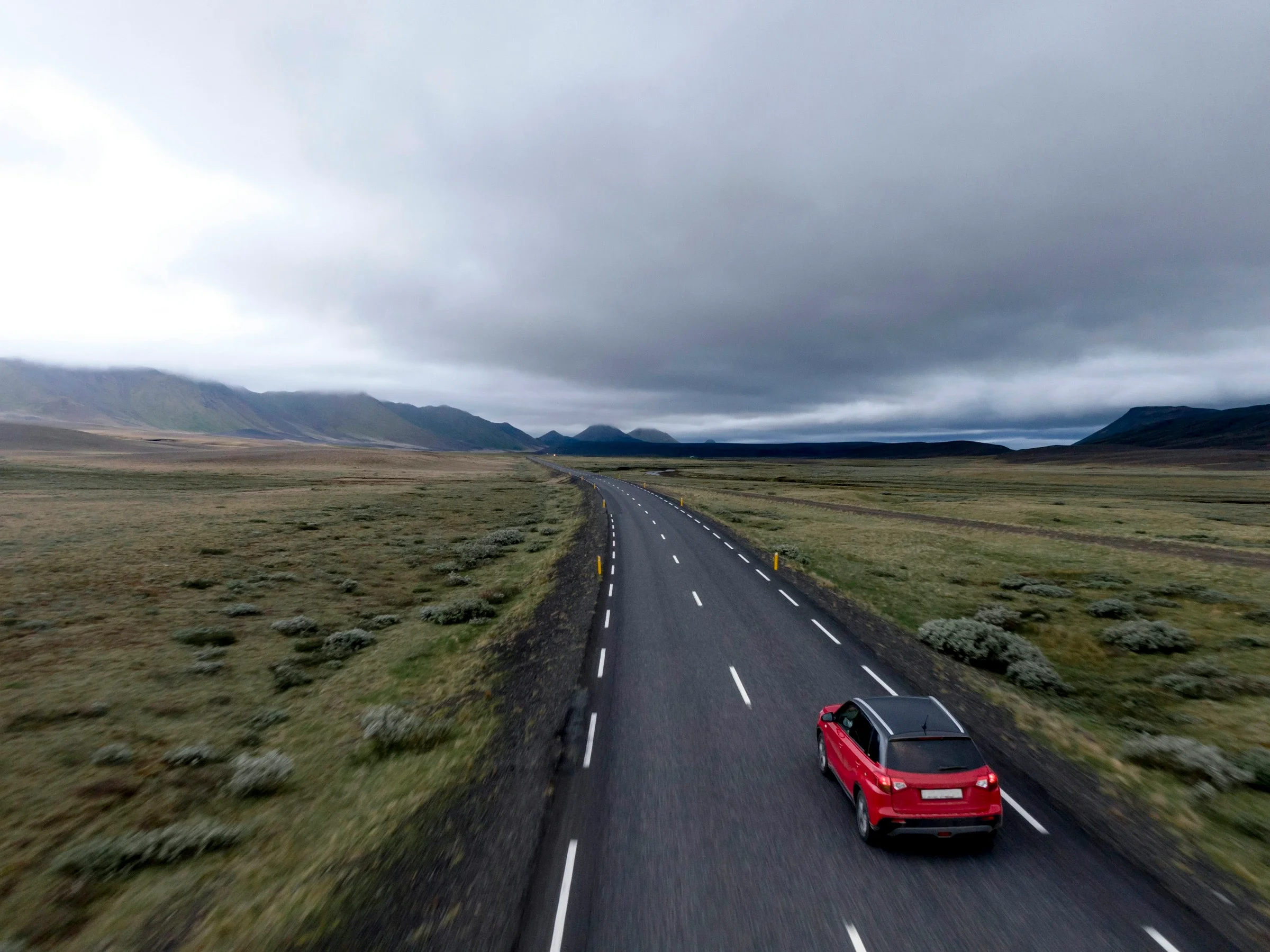 Coche rojo circulando por una carretera entre campos, visto desde arriba